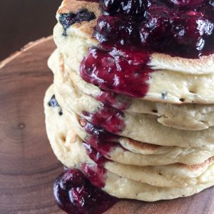 giant stack of fluffy blueberry pancakes covered in fresh berry compote