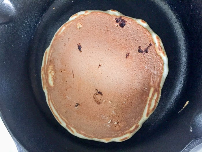 flipped blueberry pancake in cast iron skillet.