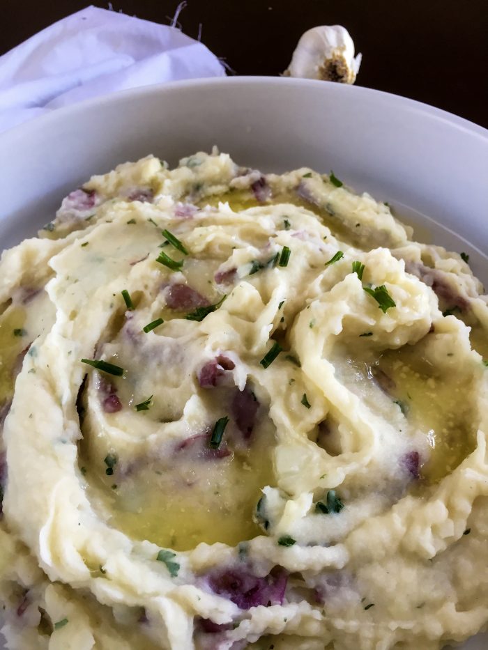 garlic mashed red potatoes garnished with chopped chive and pools of melted butter.