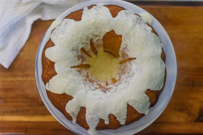 pineapple pound cake covered in vanilla frosting on cake stand.