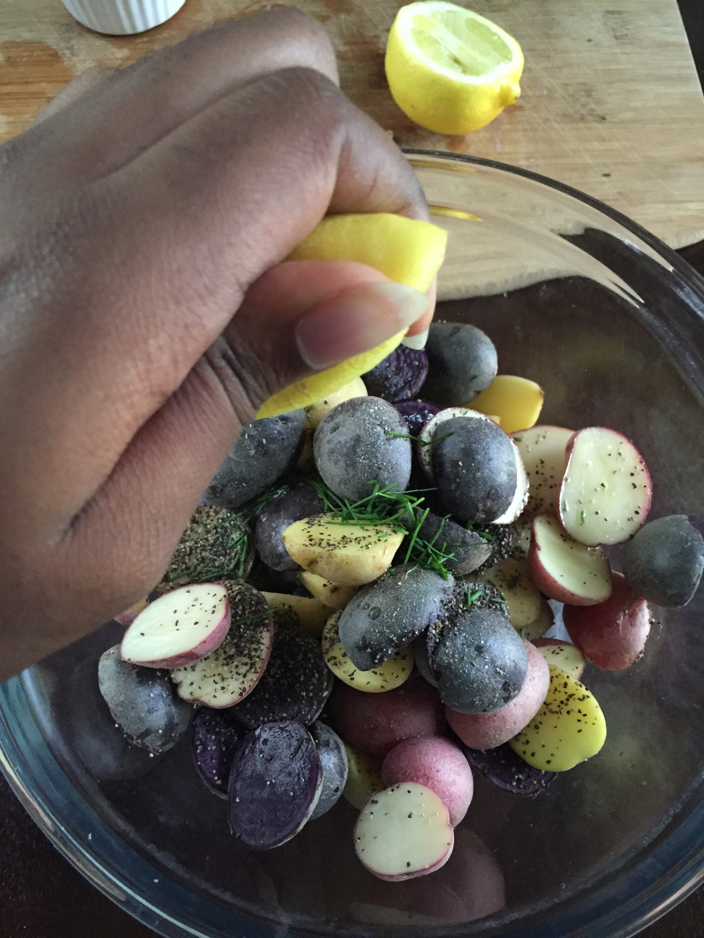 squeezing lemon over mixture of baby potatoes, herbs, and spices