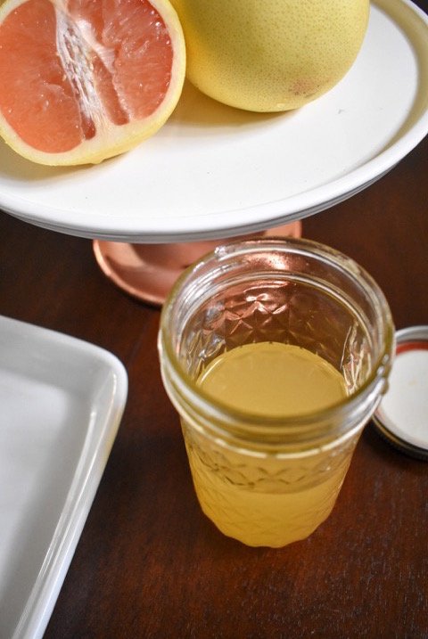 jar of homemade grapefruit simple syrup and fresh grapefruit on cake stand.