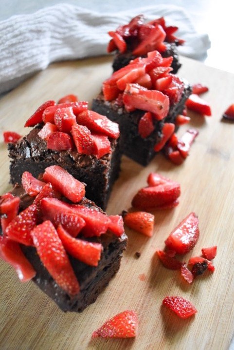 thick box mix brownies on wooden cutting board with macerated strawberries.