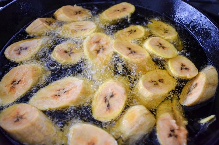 fresh plantain frying in cast iron skillet.