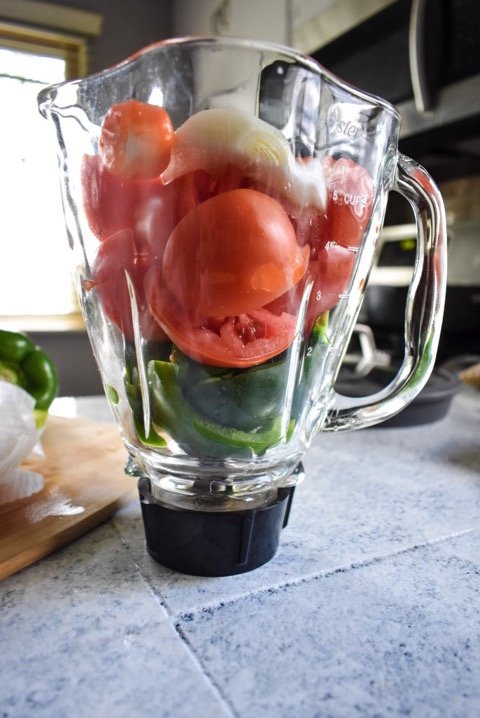 ingredients for Nigerian red stew in blender jar: cut tomatoes, green bell pepper, onion, water, and scotch bonnet peppers.