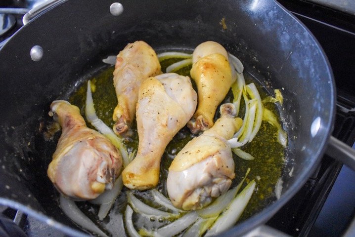 Chicken drumsticks and sliced white onions cooking in oil.