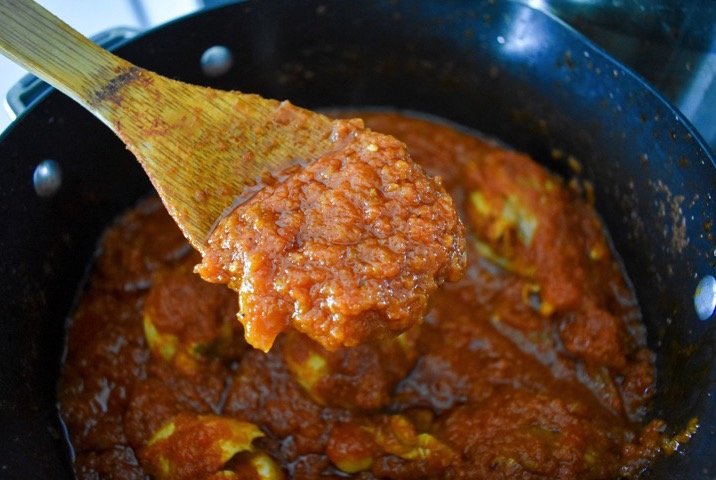 spooning cooked Nigerian red stew out of pot.
