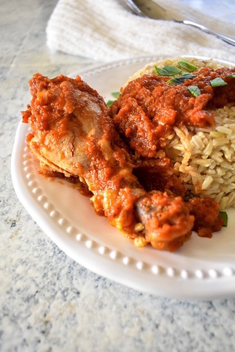 chicken drumstick and brown rice with red stew on white plate.