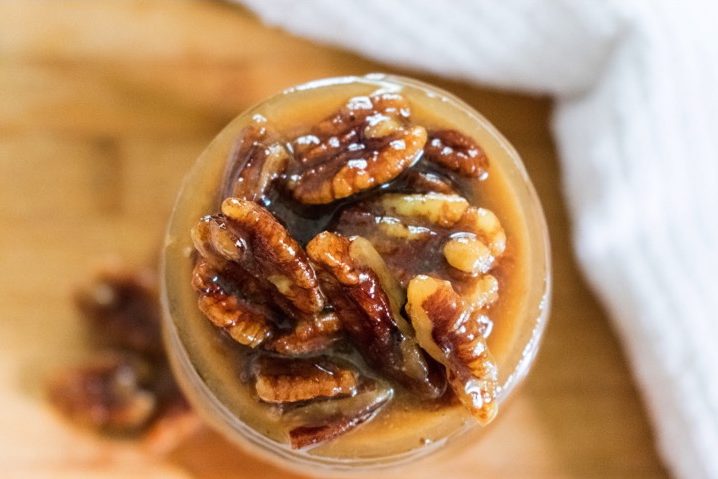 glazed pecans cresting out of jar full of southern pecan praline sauce.