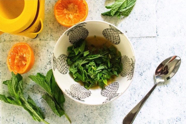 chopped mint leaves in bowl with sweet orange juice and honey