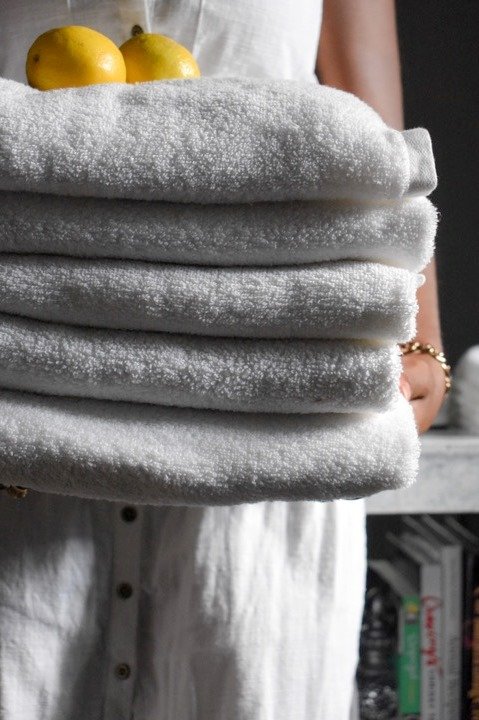 holding stack of fresh white towels and lemons
