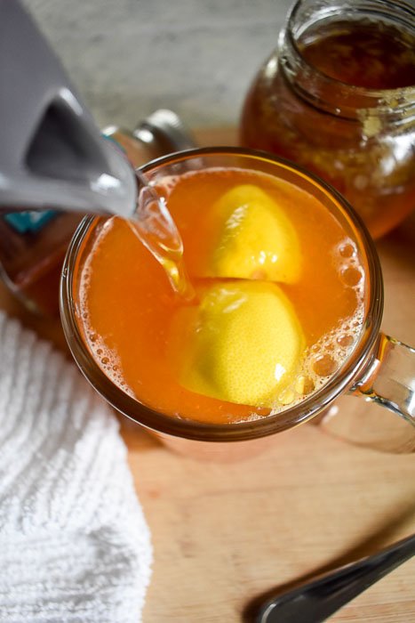 pouring warm water into a mug of lemon, honey, and cayenne pepper.