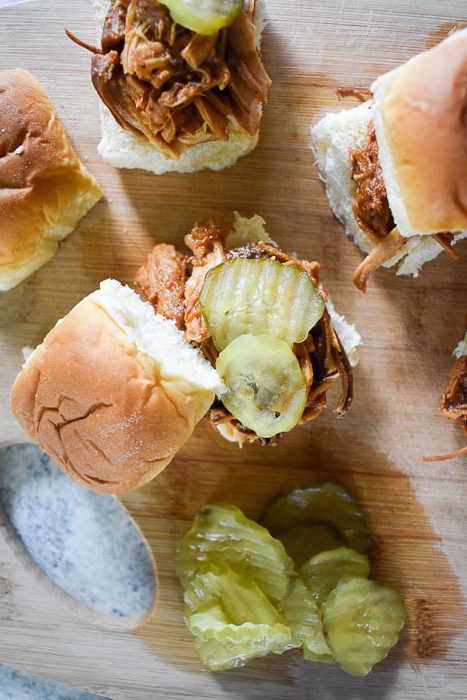 BBQ pulled chicken sliders on toasted Hawaiian rolls garnished with pickles.