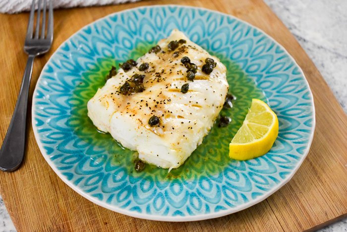 cooked cod filet topped with capers and brown butter with a lemon wedge on the side