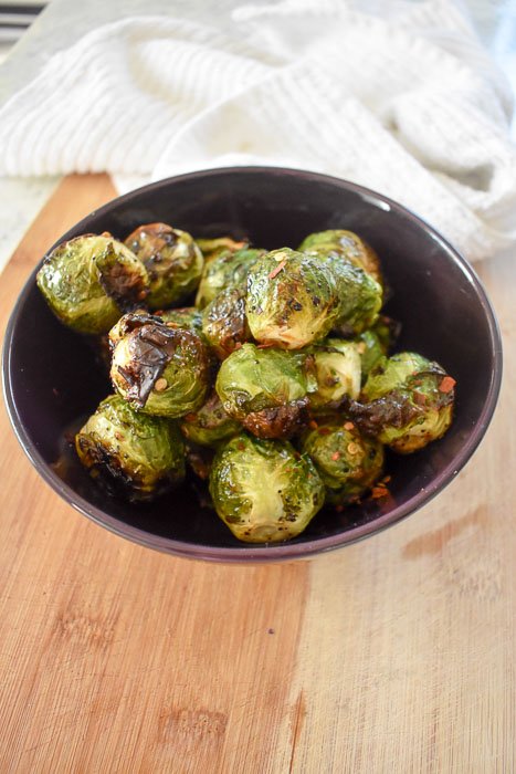 crispy roasted brussels sprouts in a bowl on top of a wooden cutting board