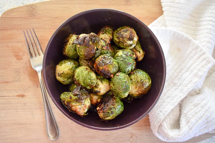 crispy roasted brussels sprouts in a bowl flanked by a fork and white kitchen towel