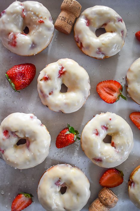 champagne glazed strawberry donuts for Valentine's Day on platter with fresh strawberries, sugar sprinkles, and champagne corks.