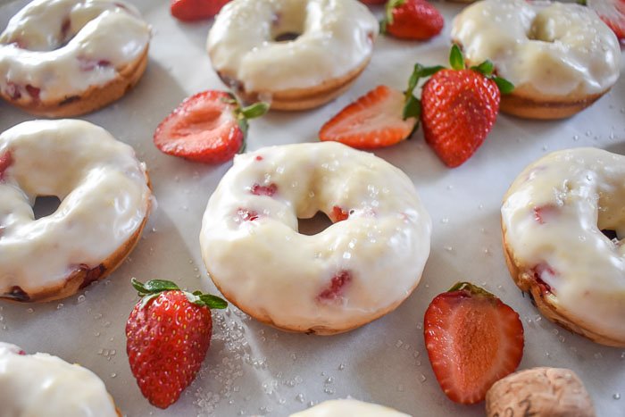 pan of glazed strawberries & champagne donuts with fresh strawberries and sugar sprinkles.