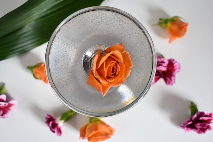 arial view of violet-colored cocktail with orange spray rose floating in it.