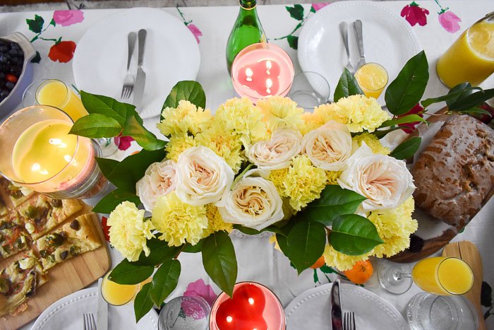centerpiece of garden roses, yellow carnations, and green leaves on a brunch tablsecape