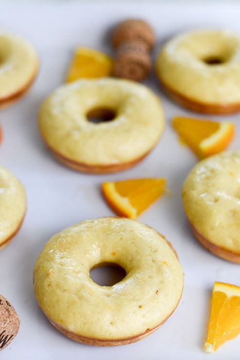baked mimosa donuts, surrounded by orange pieces and champagne corks.