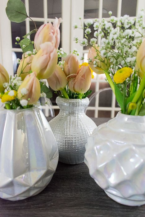 three flower arrangements in short white iridescent vases