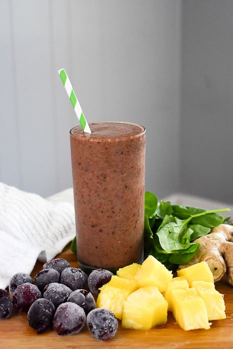 Tall cherry pineapple ginger smoothie surrounded by fresh produce