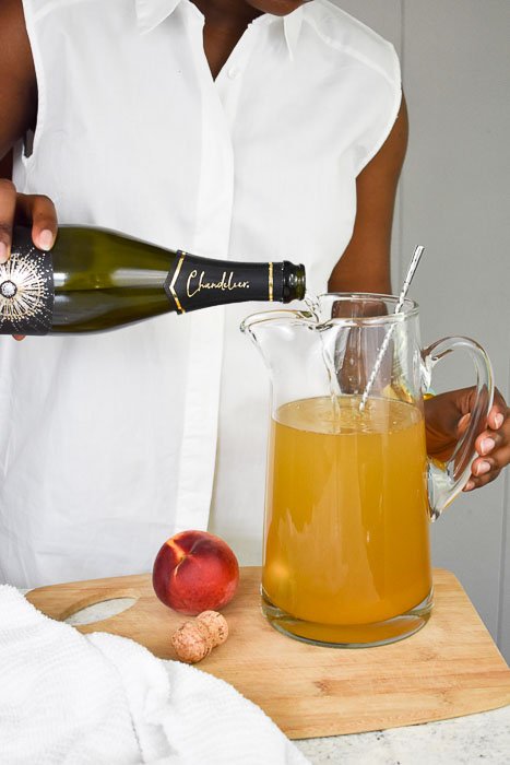 Dash of Jazz pouring sparkling wine into a pitcher of lemon ginger bellini punch