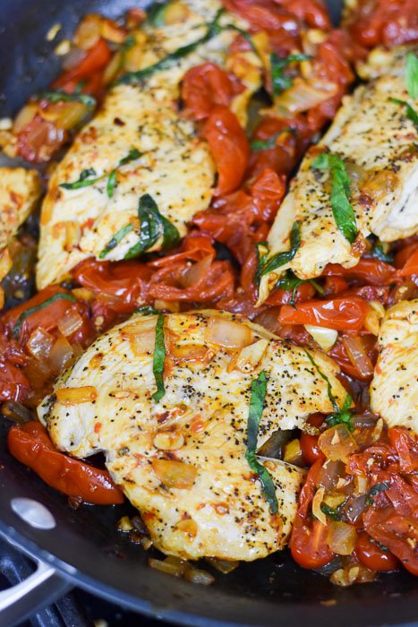 Cooked butterfly chicken breast angel tomatoes, and aromatics in a skillet.