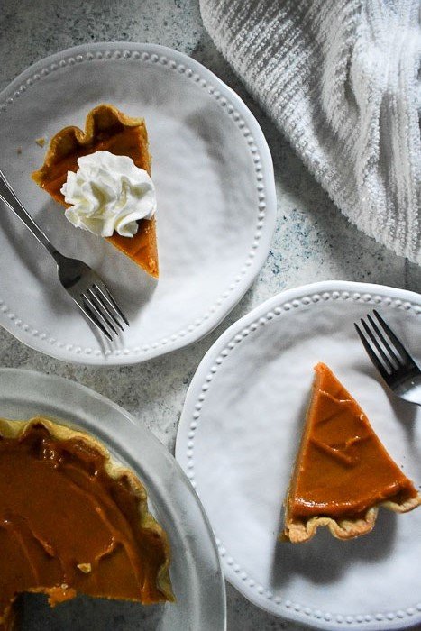 two slices of sweet potato pie on white plates with forks.