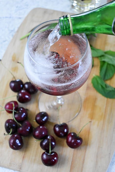 pouring sparkling water into cherry rosé spritzer glass