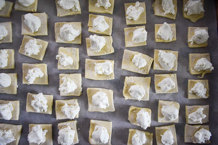 squares of puff pastry topped with goat cheese on sheet pan before baking.