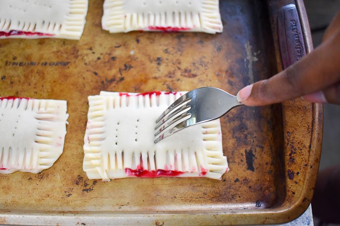 scoring unbaked homemade cherry pop tarts with fork before baking