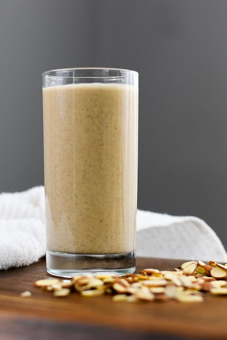 breakfast smoothie in highball glass surrounded by sliced almonds.