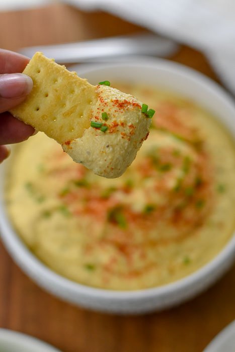 deviled egg dip garnished with fresh chive, cayenne pepper, and smoked paprika on cracker.