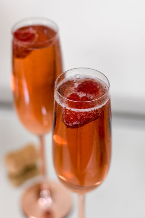 two whiskey champagne cocktails with fresh raspberries.