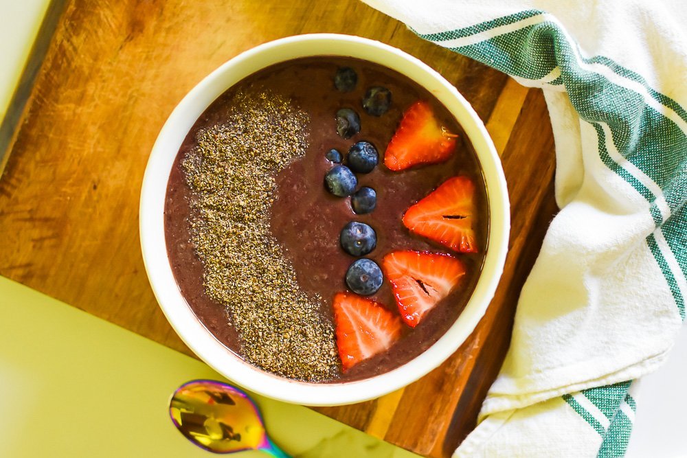 Acai smoothie bowl garnished with milled chia seeds, fresh blueberries, and strawberry slices.