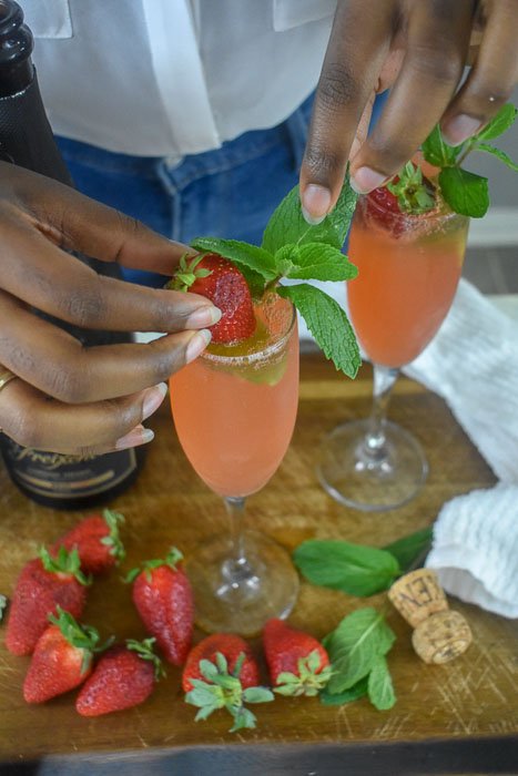garnishing strawberry mint mimosa with fresh strawberry and sprig of mint leaves.