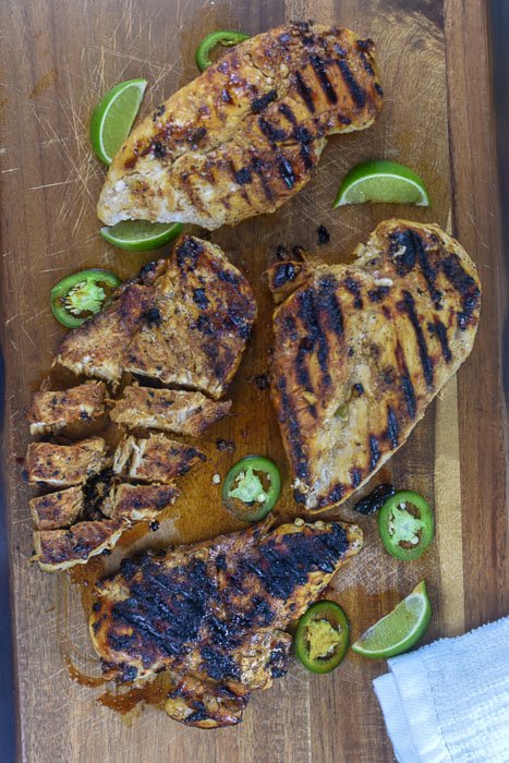 four grilled chicken breasts with slices of jalapeño and lime on cutting board.