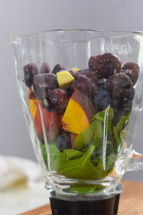 frozen cherries, ginger, peach, blueberries, and spinach leaves in blender