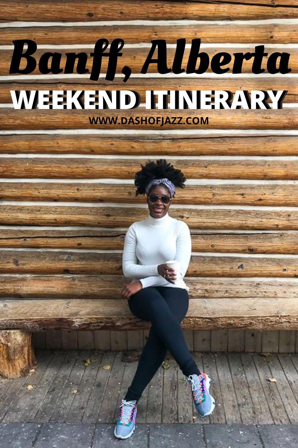 Jazzmine sitting in front of log cabin wall holding coffee with text overlay "Banff, Alberta weekend itinerary"
