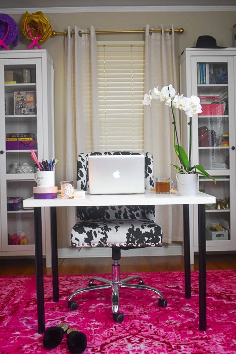 colorful home office setup with pink rug, desk, and cow print chair