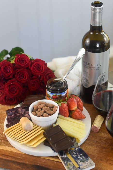 romantic cheese plate for two served next to a bouquet of red roses and uncorked bottle of red wine.
