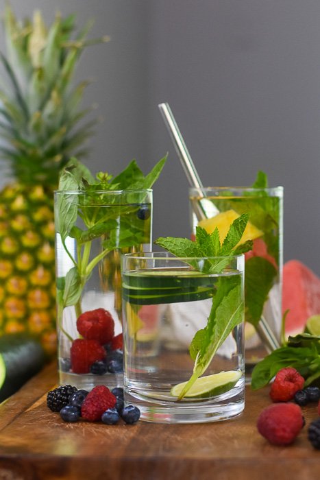 three glasses of infused water surrounded by fresh fruits