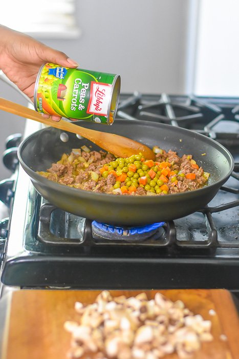 pouring Libby's peas and carrots into skillet of shepherd's pie filling.