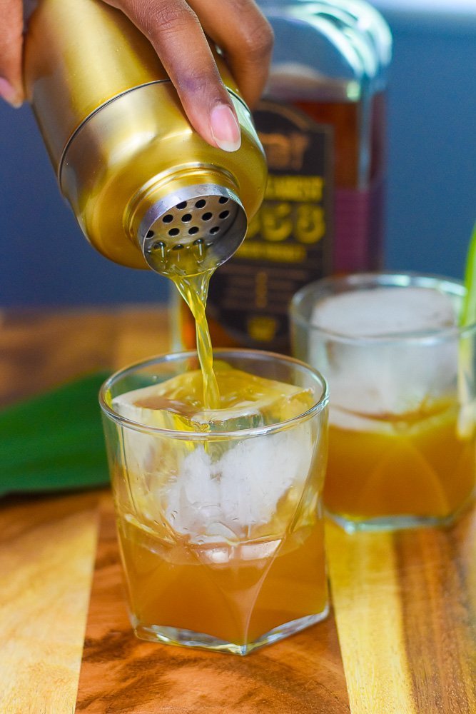 pouring brown sugar pineapple whiskey sipper from cocktail shaker over ice