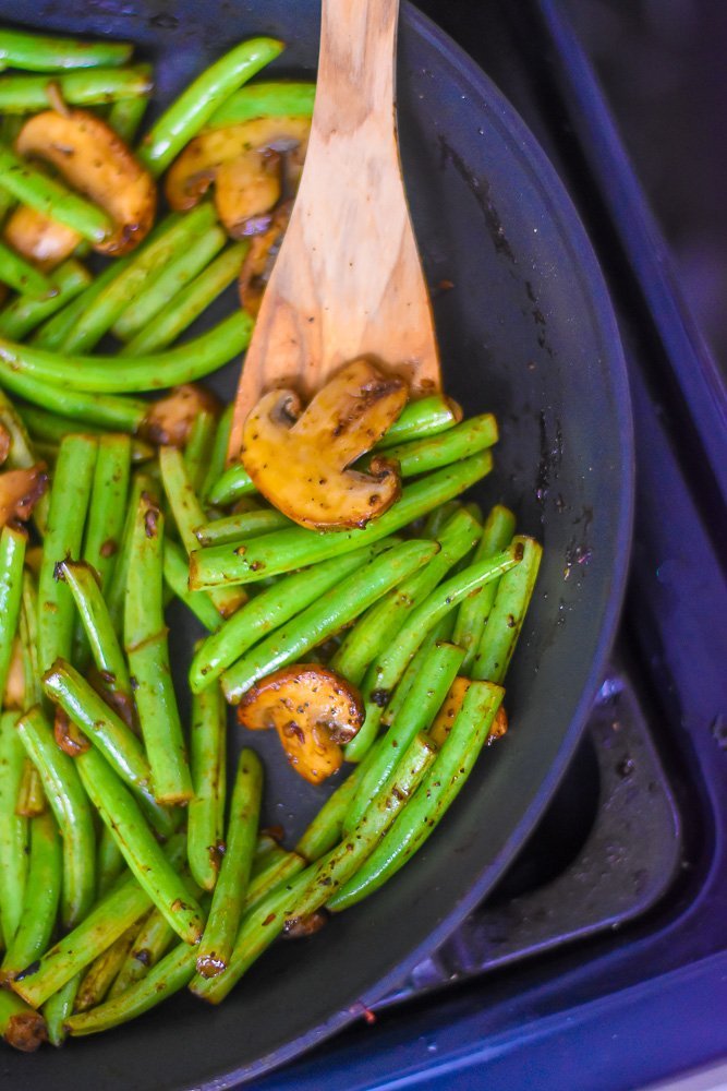 cooked fresh green beans and mushrooms in skillet with wooden kitchen spoon.