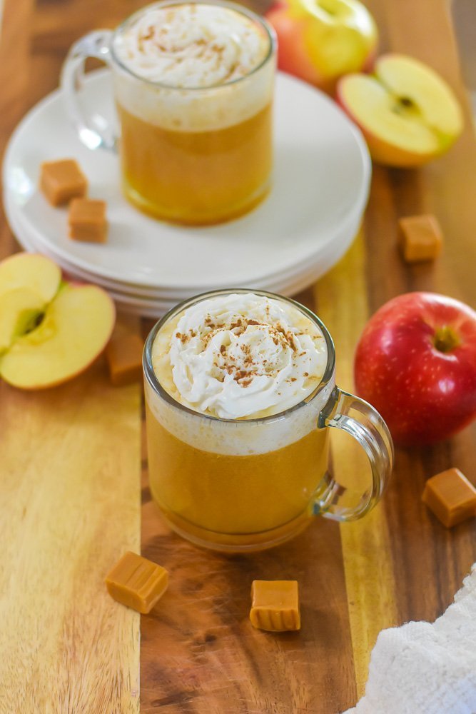 mug of bourbon caramel apple cider surrounded by apples and caramel candy.
