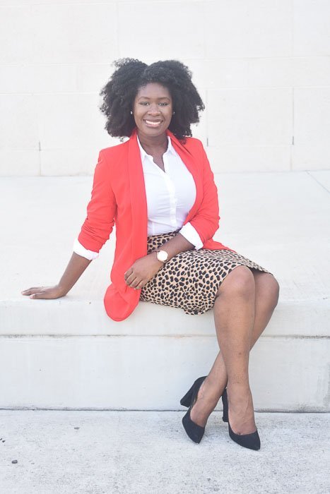 Jazzmine seated outdoors, wearing natural afro hair with a business professional outfit.