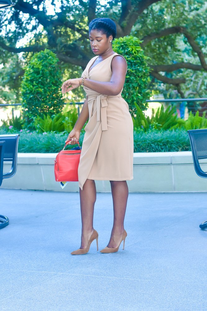 Jazzmine standing outdoors looking down at watch, wearing camel wrap dress, and natural hair in simple flat twist.